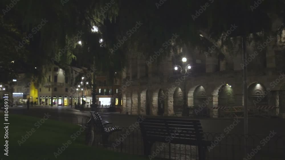 Wall with arches illuminated at night, lights of cafes across deserted street Wall with arches illuminated at night, lights of cafes across deserted street