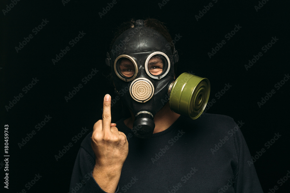 Man in gas mask shows middle fingers sign on dark background Man in gas mask shows middle fingers sign on dark background