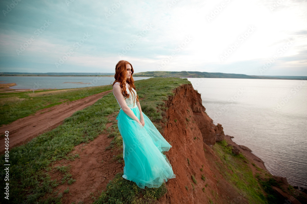 beautiful young girl with red hair in a lavish dress walking in the nature near the lake beautiful young girl with red hair in a lavish dress walking in the nature near the lake