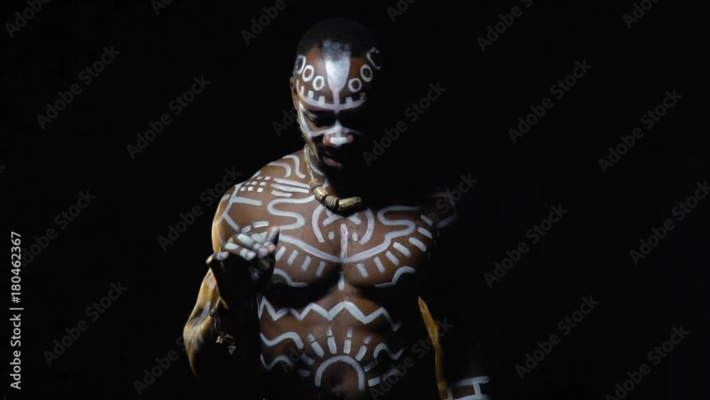 A muscular black man in white patterns beats the rhythm with his fingers in the dark