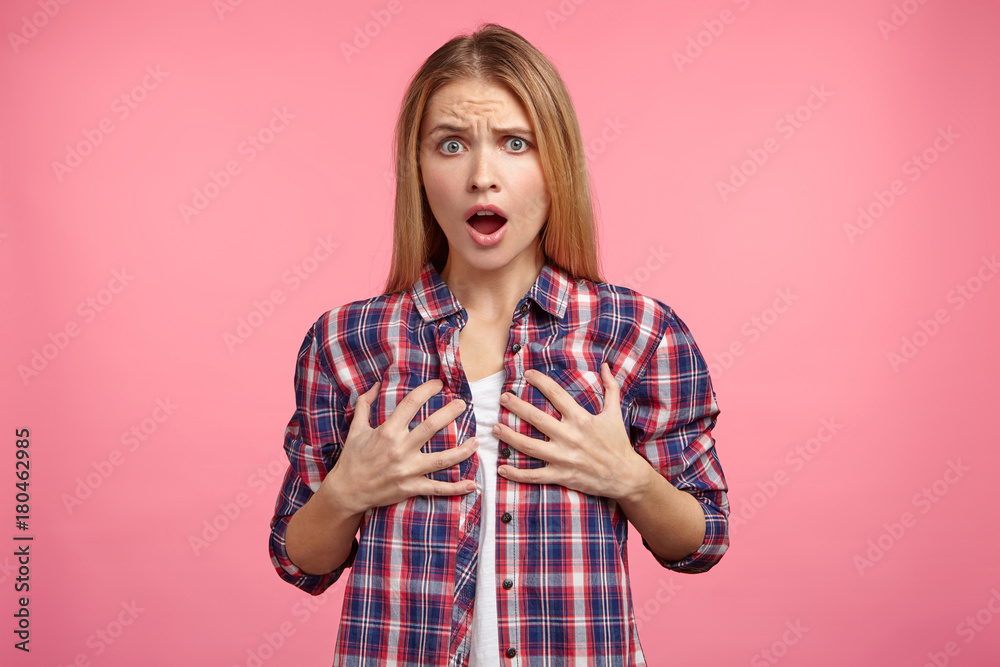 Studio shot of discontent female keeps hands on breast, displeased to hear bad comments from men, talking about her bosom size. Unhappy beautiful woman with shocked expression, isolated on pink Studio shot of discontent female keeps hands on breast, displeased to hear bad comments from men, talking about her bosom size. Unhappy beautiful woman with shocked expression, isolated on pink