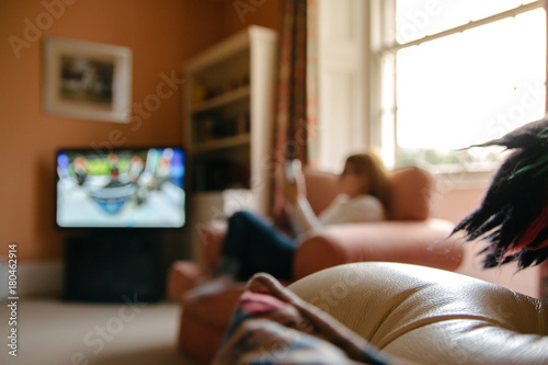 blurred out image of a woman relaxing in a sitting room looking at her mobile phone with light streaming in from a large window