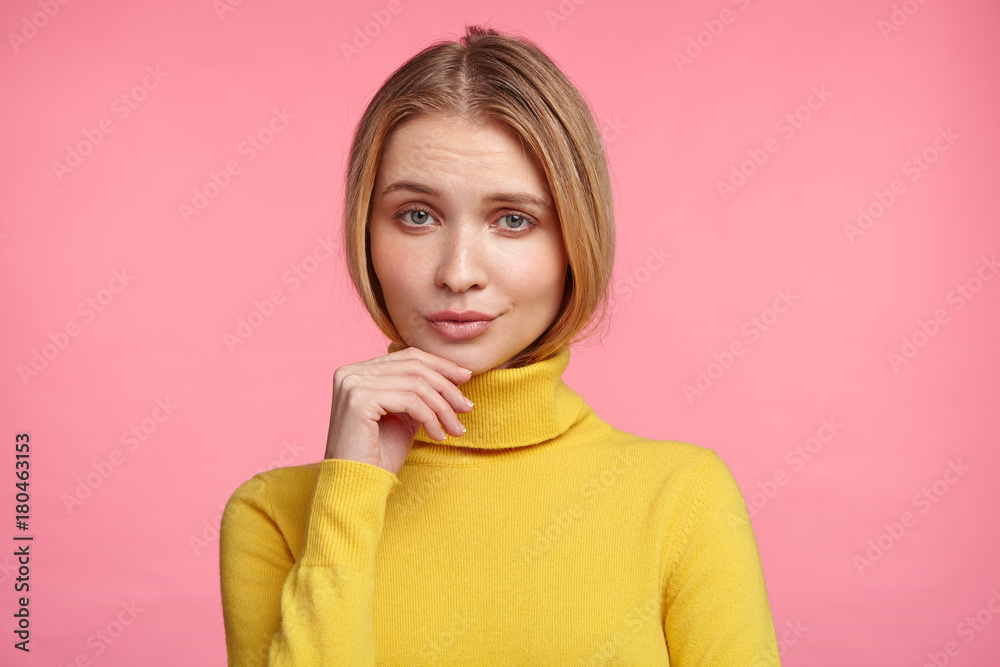Confident serious pleasant looking young female model dressed casually, looks directly into camera, listens to interlocutor very attentively, analyzes information in her mind, isolated over pink wall Confident serious pleasant looking young female model dressed casually, looks directly into camera, listens to interlocutor very attentively, analyzes information in her mind, isolated over pink wall