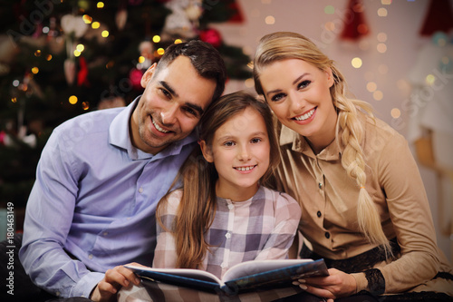 Family reading story book together under Christmas tree