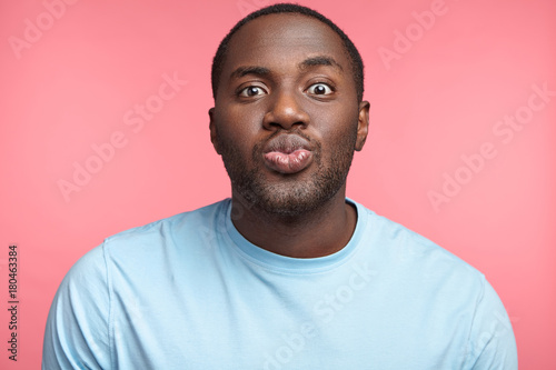 Canvas Print Pleasant looking African American man rounds lips, going to recieve kiss from beautiful girl, being in anticipation of pleasant moment