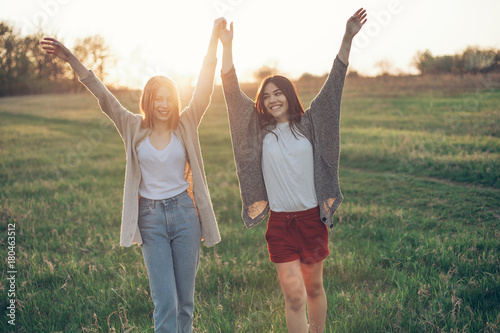 Two young women with raised hands under the sunset light