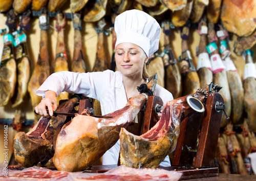 Woman in uniform slicing delicious prosciutto meat