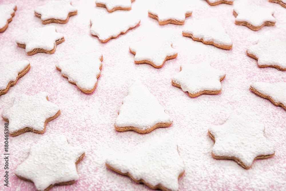 Christmas gingerbread pattern, top view, flat lay. Cookies covered with white icing and powdered sugar in pale pastel colors shaped as fir-tree and star. Pink wooden background