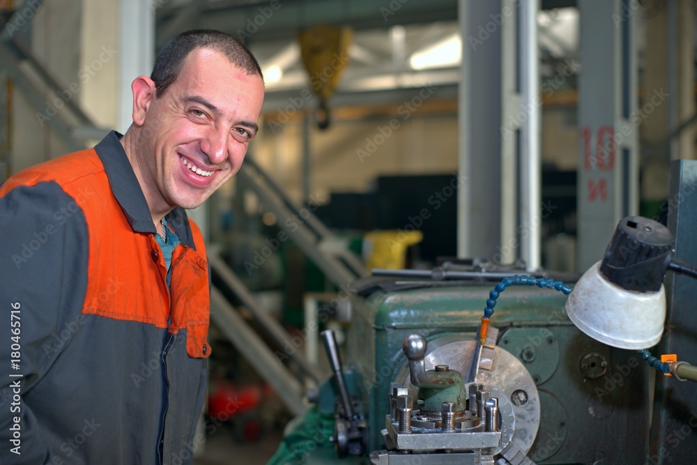 metalworking industry: factory man worker in uniform working on lathe machine in workshop