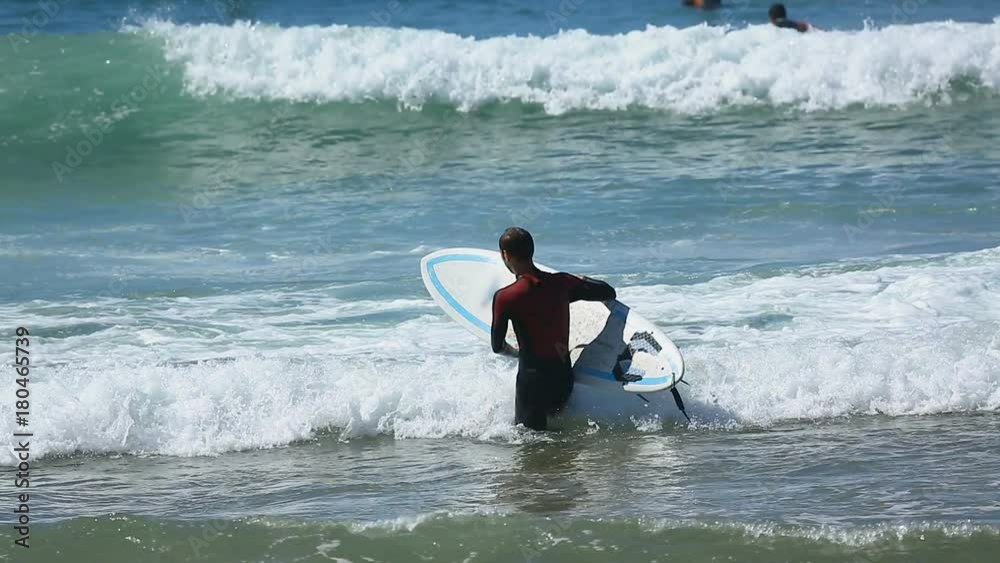 Man in surfing costume entering ocean, carrying board in hands, active sport Man in surfing costume entering ocean, carrying board in hands, active sport