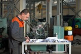 metalworking industry: factory man worker in uniform working on lathe machine in workshop