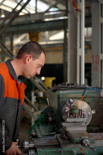 metalworking industry: factory man worker in uniform working on lathe machine in workshop