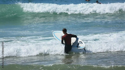 Man in surfing costume entering ocean, carrying board in hands, active sport
