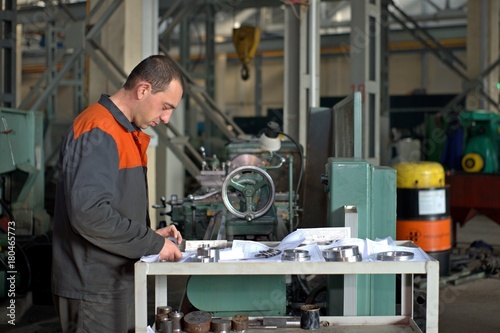 metalworking industry: factory man worker in uniform working on lathe machine in workshop