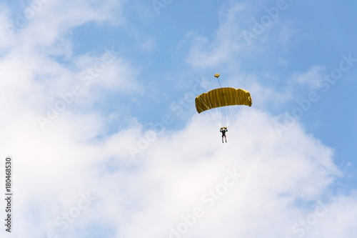 Parachutist skydiving with open yellow parachute clouds blue sky background