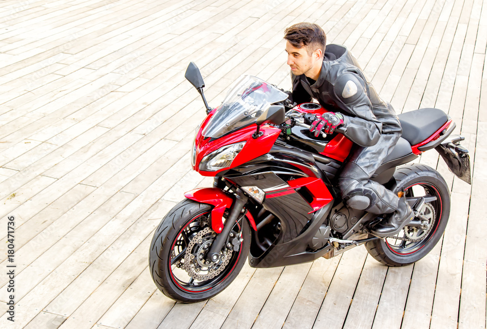 Obraz premium Handsome rider guy in black leather biker jacket ride on classic style racer motorbike.