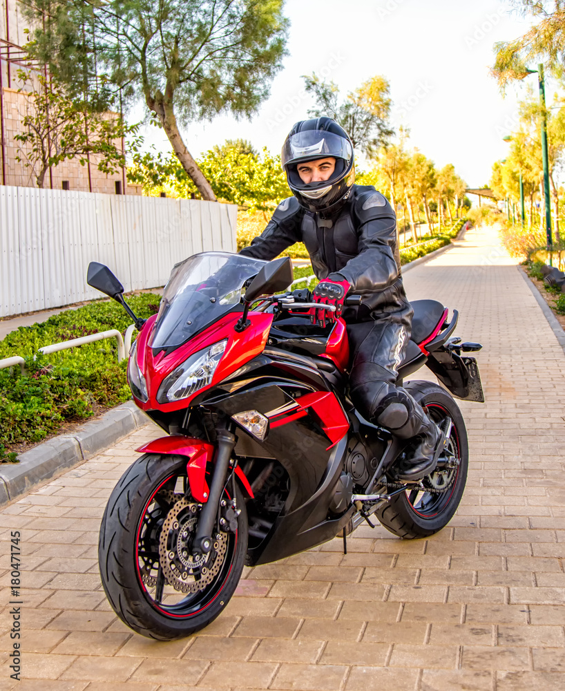 Fototapeta premium Handsome rider guy in black leather biker jacket and helmet ride on classic style racer motorbike.