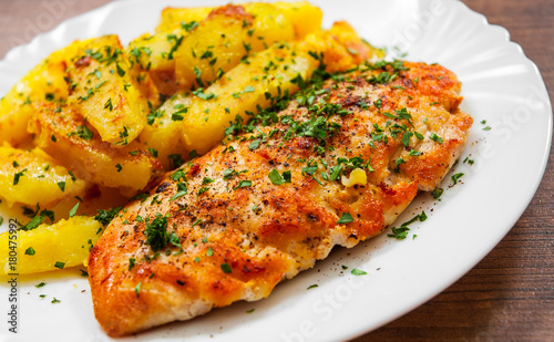 Grilled chicken breast with potato in a plate on a wooden background.