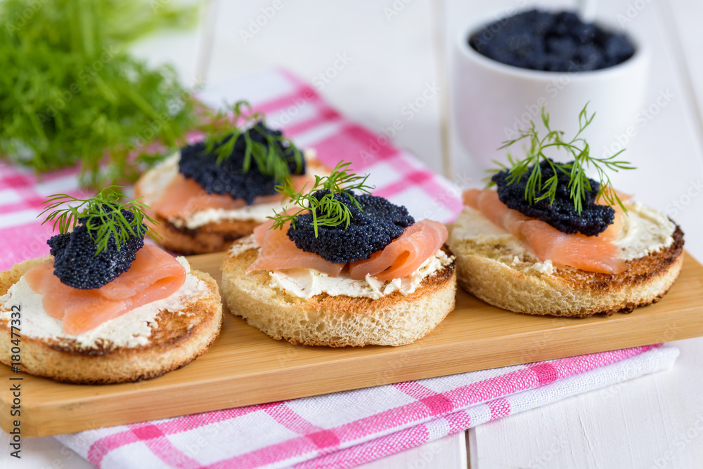 Appetizer toast bread with cream cheese, smoked salmon and black caviar decorated by dill.