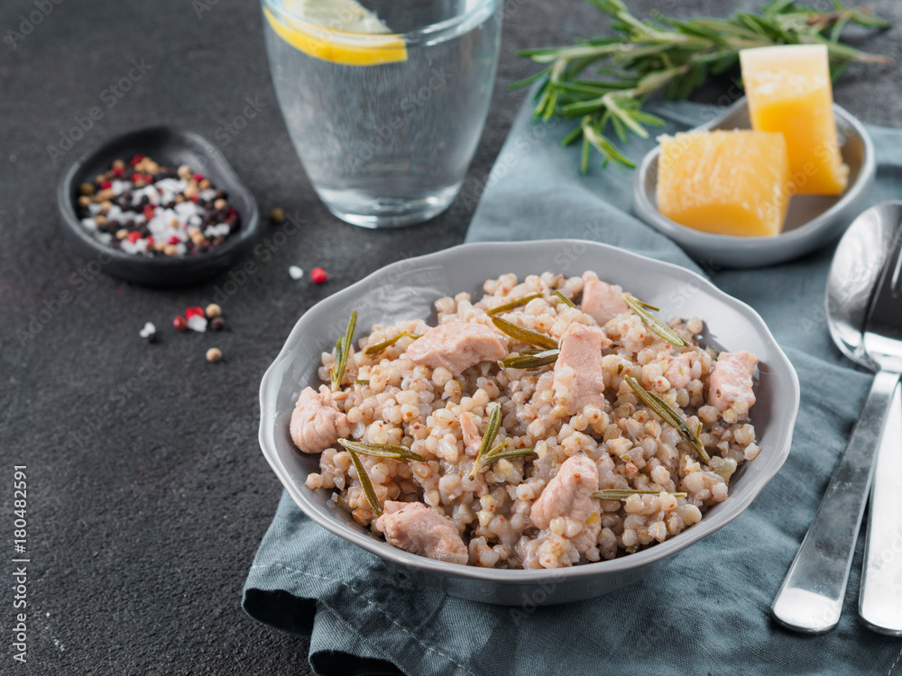 Raw buckwheat risotto with chicken meat and rosemary served parmesan cheese in gray plate on black cement background. Gluten-free and buckwheat recipe ideas. Copy space Raw buckwheat risotto with chicken meat and rosemary served parmesan cheese in gray plate on black cement background. Gluten-free and buckwheat recipe ideas. Copy space