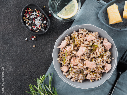 Raw buckwheat risotto with chicken meat and rosemary served parmesan cheese in gray plate on black cement background. Gluten-free and buckwheat recipe ideas. Copy space. Top view or flat-lay.