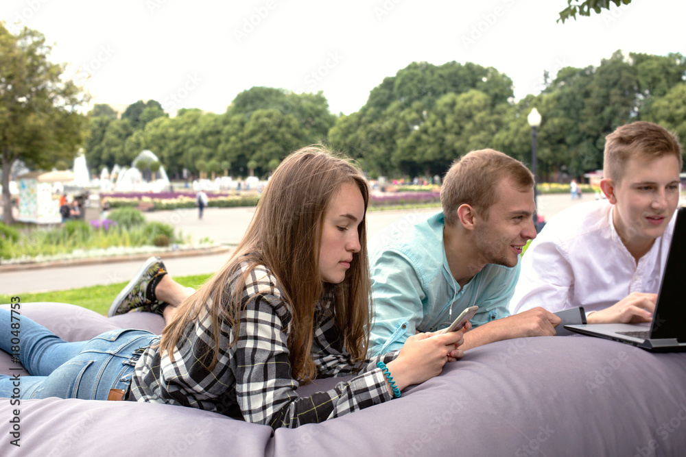 Three young friends relaxing outdoors in the park on a big cushion. Three young friends relaxing outdoors in the park on a big cushion.