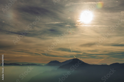 View on the sky with clouds and sun that shines bright over the Dolomiti mountains covered in fog  Trentino  Italy