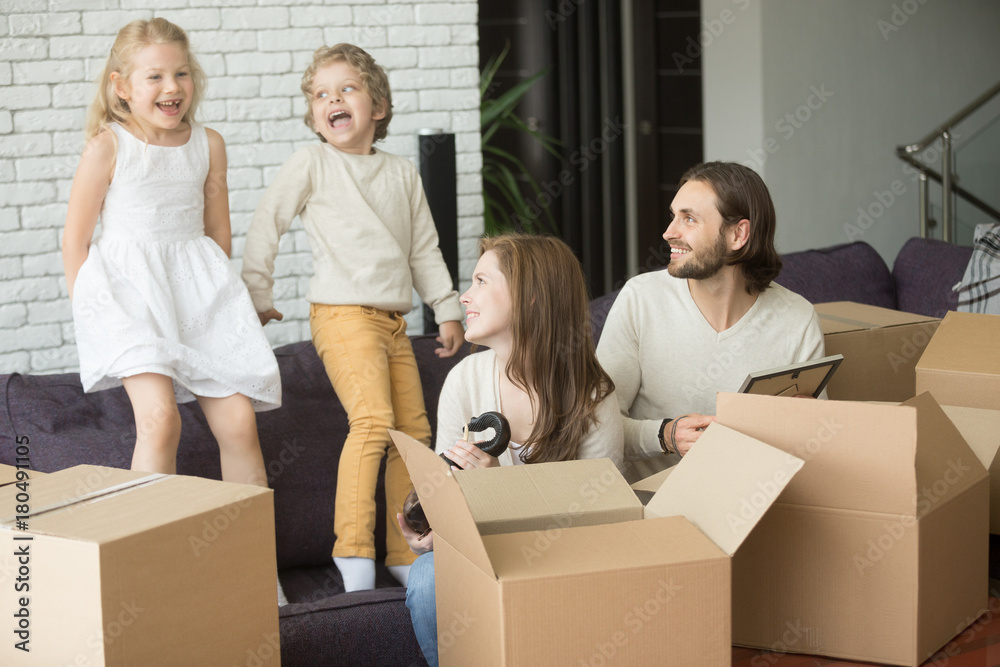 Happy excited young family with kids playing in new home living room on couch, father mother and children having fun on sofa unpacking cardboard boxes together, moving into house relocation concept Happy excited young family with kids playing in new home living room on couch, father mother and children having fun on sofa unpacking cardboard boxes together, moving into house relocation concept