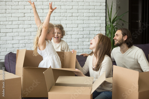 Happy child girl jumping out of cardboard box, family playing with kids in living room on sofa, parents and children laughing having fun together at moving day, move in new home or relocating concept © fizkes