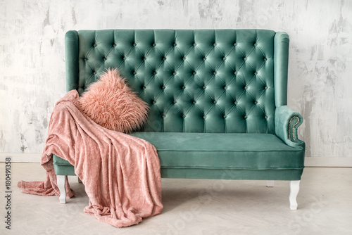 Gray-blue sofa on the background of a white wall. Pink pillow of artificial fur and blanket