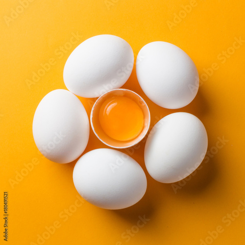 White eggs and egg yolk on the yellow background. topview, square