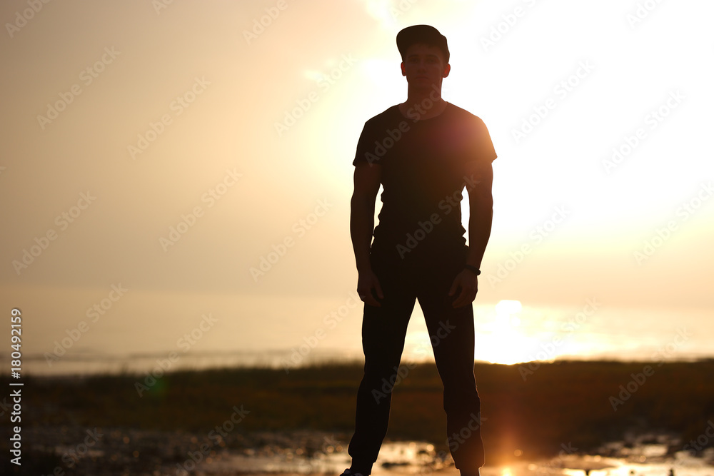 Silhouette of man standing on beach in the sunset at the sea.