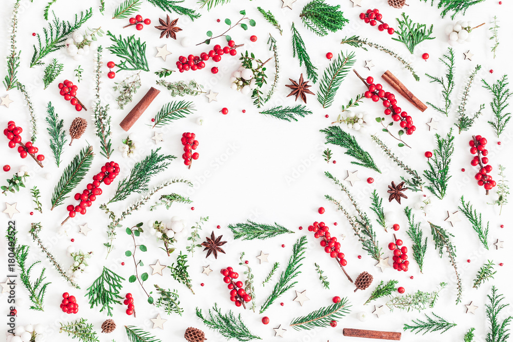 Christmas composition. Frame made of christmas tree branches, red berries, cinnamon sticks, anise stars, decorations on white background. Flat lay, top view, copy space