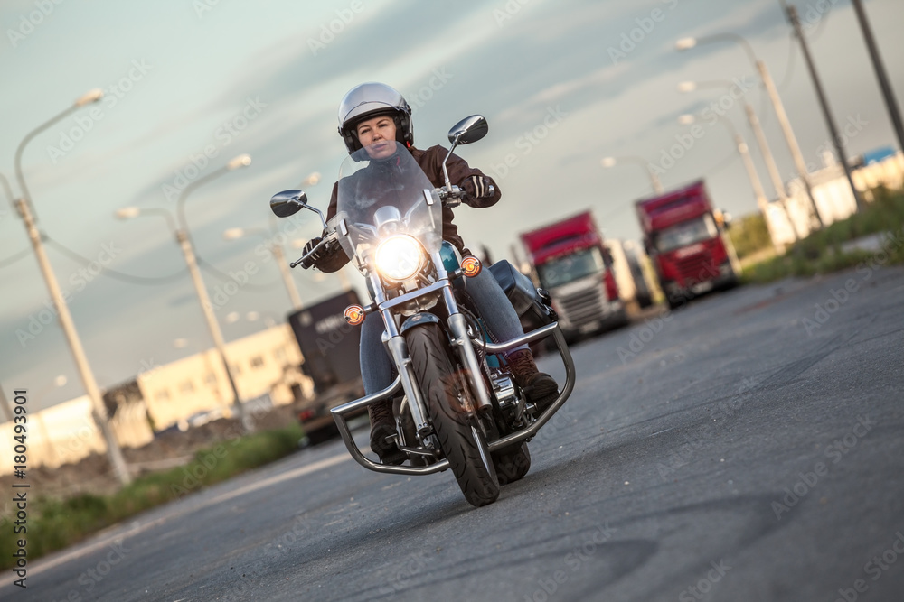Obraz premium Kobieta motocyklista jazda na chopperze z włączaniem reflektorów na asfaltowej drodze miejskiej