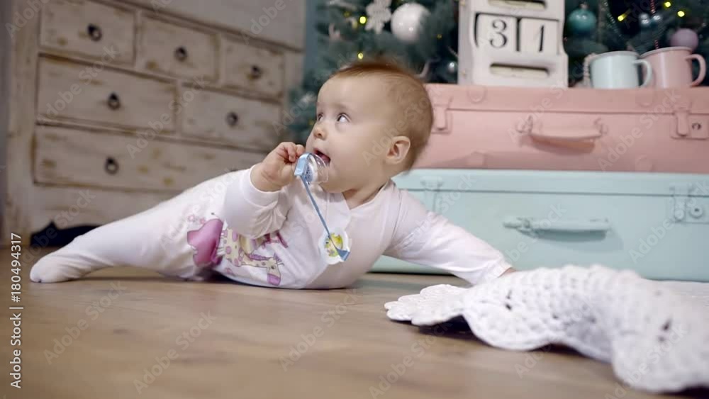 girl kid in white overalls crawling on the floor in a Christmas interior with a pacifier in his hands girl kid in white overalls crawling on the floor in a Christmas interior with a pacifier in his hands