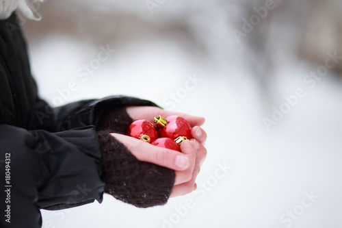 hands of a child holding three red Christmas toys on the background of a snow-covered city. Vertical orientation