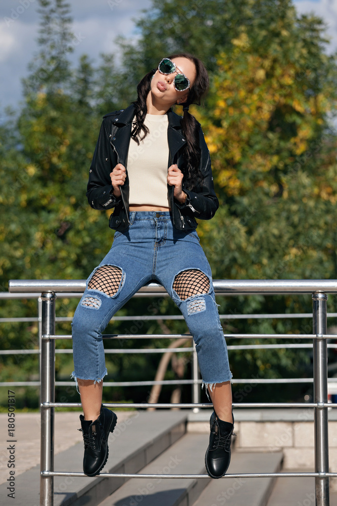 fashionable young woman in rock style clothes, black leather jacket, blue  jeans, tights in a grid under battered jeans Stock Photo | Adobe Stock