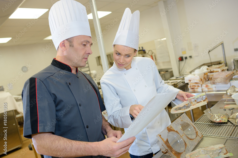 male assistant and woman chef preparing food in commercial kitchen