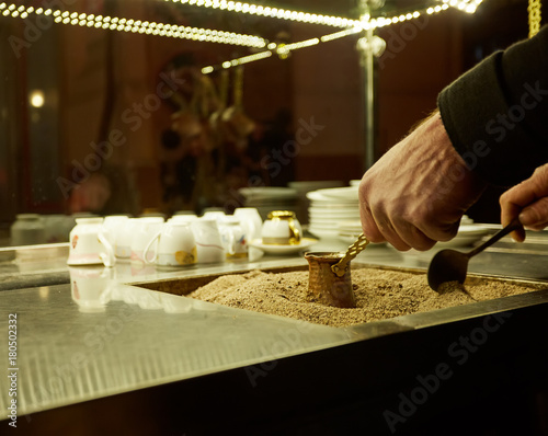 Close up hands of a man cooking turkish coffee on hot golden sand. photo