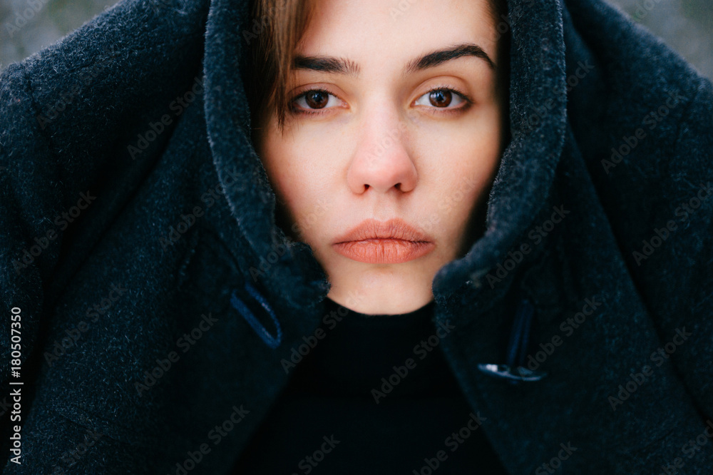 Unusual female portrait. Unique person closeup expressive face. Young serious girl in winter outdoor. Odd bizarre woman with bang on forehead. Winter frost cold day at nature. Coat on head. Headdress. Unusual female portrait. Unique person closeup expressive face. Young serious girl in winter outdoor. Odd bizarre woman with bang on forehead. Winter frost cold day at nature. Coat on head. Headdress.