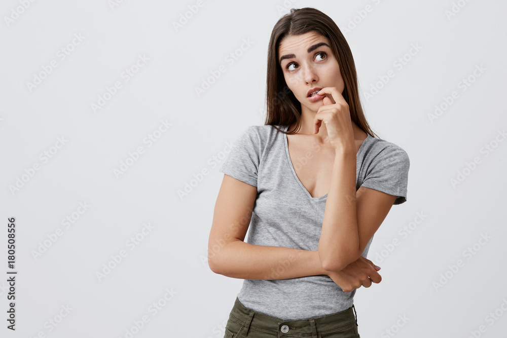 Thinking about presents for Christmas. Portrait of young good-looking sexy caucasian girl with dark long hair in fashionable casual outfit holding hand near lips, looking aside with thoughtful Thinking about presents for Christmas. Portrait of young good-looking sexy caucasian girl with dark long hair in fashionable casual outfit holding hand near lips, looking aside with thoughtful