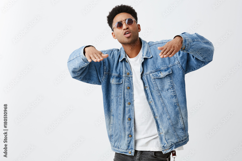 Young attractive black-skinned man with dark curly hair in white t-shirt,  denim jacket and sun-glasses gesticulating with hands, rapping with friends  on party. Copy space Stock Photo | Adobe Stock