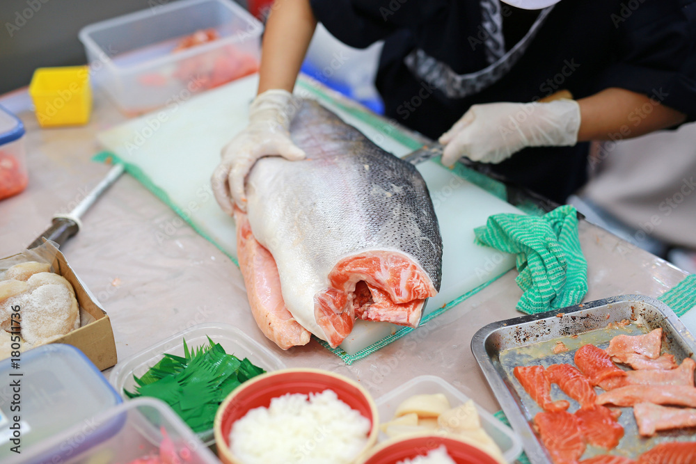 Japanese chef slicing raw fish for salmon sushi. Chef preparing a fresh salmon on a cutting board.