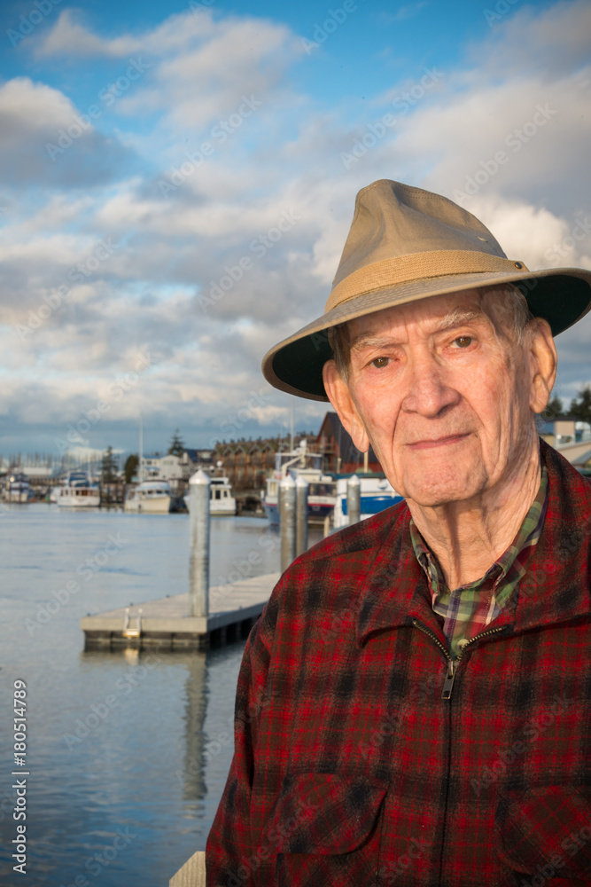 Portrait Healthy Active Elderly Man Casually Dressed with Hat Outdoors by a Marina.  Vertical. Copy space.