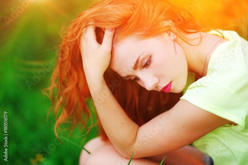 Wonderful portrait of a charming pensive red-haired girl resting in summer Park on green grass, closeup.