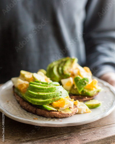 Whole grain toasts with avocado, egg, cucumber. A useful delicious breakfast. Heart from avocado. Atmospheric photo with hands Place for text, top view photo
