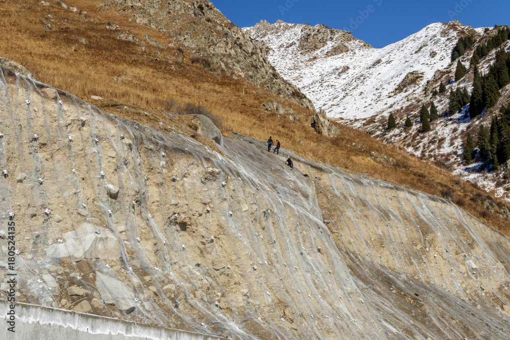 Workers strengthen the slope of the mountain with a metal net from shedding along the mountain road Workers strengthen the slope of the mountain with a metal net from shedding along the mountain road
