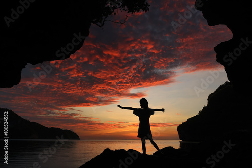 Silhouette girl standing and stretch the arms on the rocks red sky sunset background