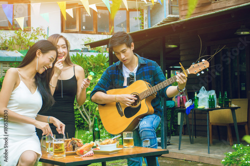 Two asian woman and one men,are smile.have fun,playing guitar.Group celebration party eating happy, concept .In garden home