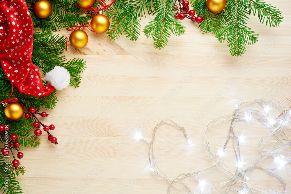 Christmas background decoration with lights, balls, santa hat and fir tree branches flat lay on wooden texture. Top view with blank space. Christmas background decoration with lights, balls, santa hat and fir tree branches flat lay on wooden texture. Top view with blank space.